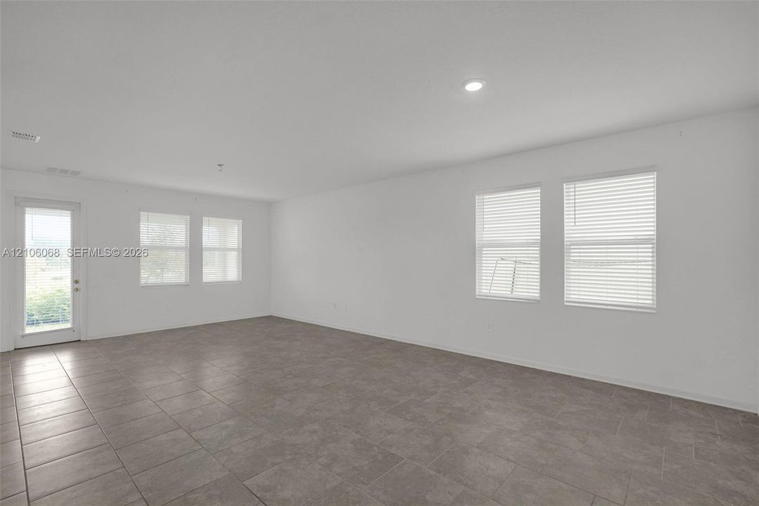 Neutral-toned tile flooring, recessed ceiling lighting, and multiple windows with horizontal blinds featuring neutral wall finishes and a glass-paneled exterior door