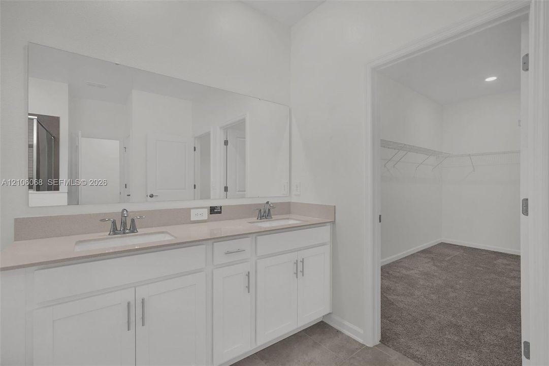 Double vanity featuring white cabinetry, quartz-surface countertops, integrated dual sinks, and a full-width wall mirror