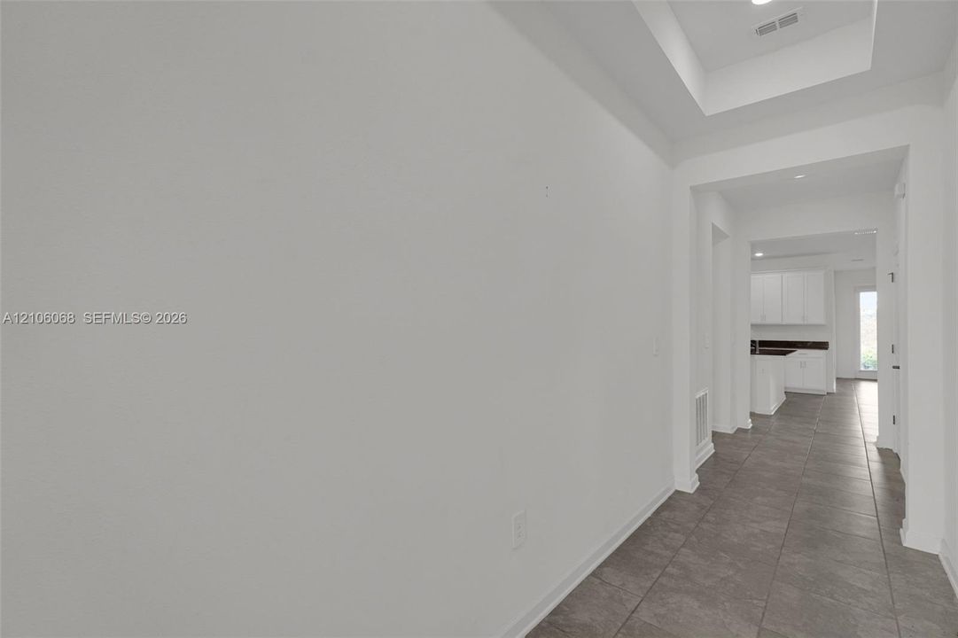 Interior hallway featuring neutral ceramic tile flooring and a recessed tray ceiling with inset lighting