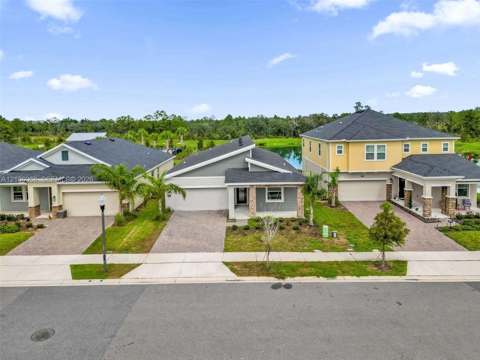 Single-story residence featuring a gray exterior finish, a stone-accented entryway, a paved driveway, and an attached multi-car garage, set against a backdrop of water and greenery