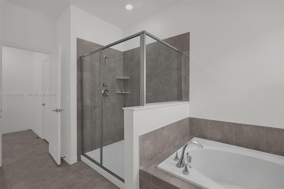 Walk-in shower with a glass enclosure, built-in shelving, and neutral tile surround, featuring a soaking tub with a deck-mounted chrome faucet and matching tile backsplash