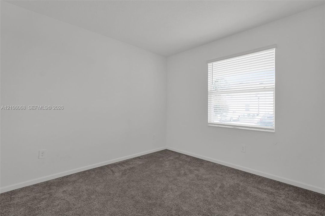 Room featuring neutral-toned carpeting, crisp white wall finishes, and a single-hung window with horizontal blinds