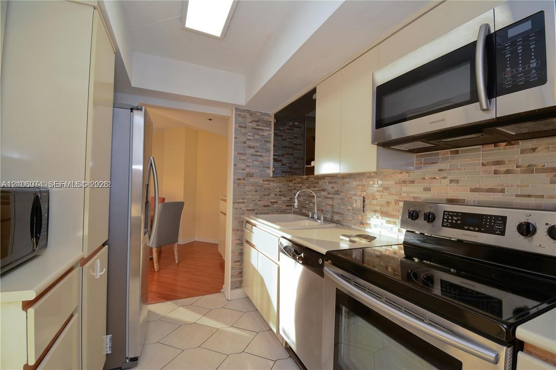 Kitchen featuring flat-panel cabinetry, stainless steel appliances, multi-tonal stacked stone backsplash, solid surface countertops, and diagonal ceramic tile flooring