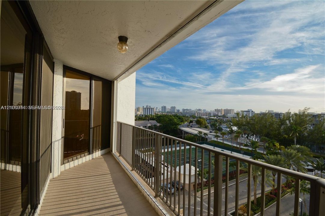 Covered balcony featuring metal railings, neutral textured flooring, ceiling-mounted lighting, and floor-to-ceiling glass sliding doors