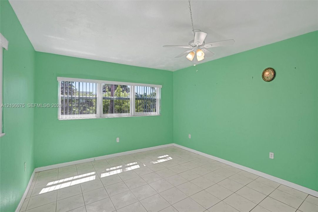 Room featuring light-toned tile flooring, a horizontal multi-pane window with vertical blinds, and a white ceiling fan with integrated lighting