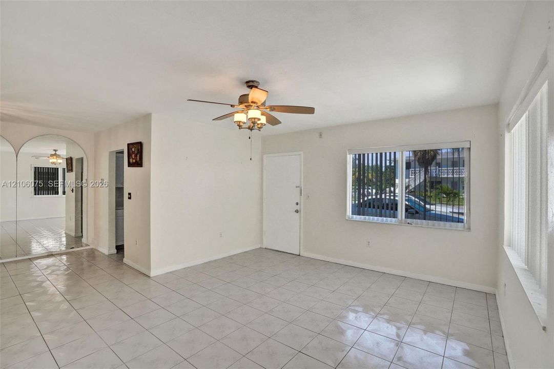 Living area featuring ceramic tile flooring, ceiling fan with integrated lighting, full-wall mirrored accent, and large windows with vertical blinds