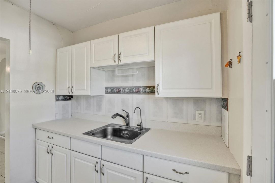 White cabinetry with metallic hardware, solid surface countertops, stainless steel single-basin sink with a gooseneck faucet, and decorative tile backsplash