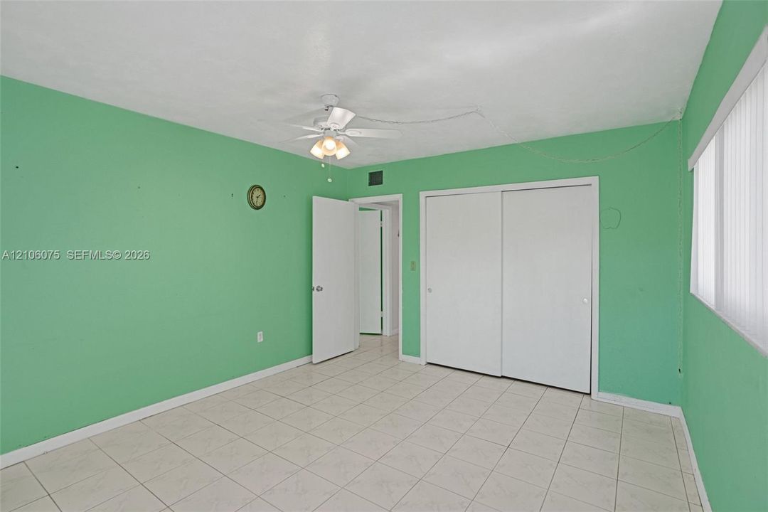 Room featuring ceramic tile flooring, ceiling fan with integrated lighting, dual-panel sliding closet doors, and vertical window blinds
