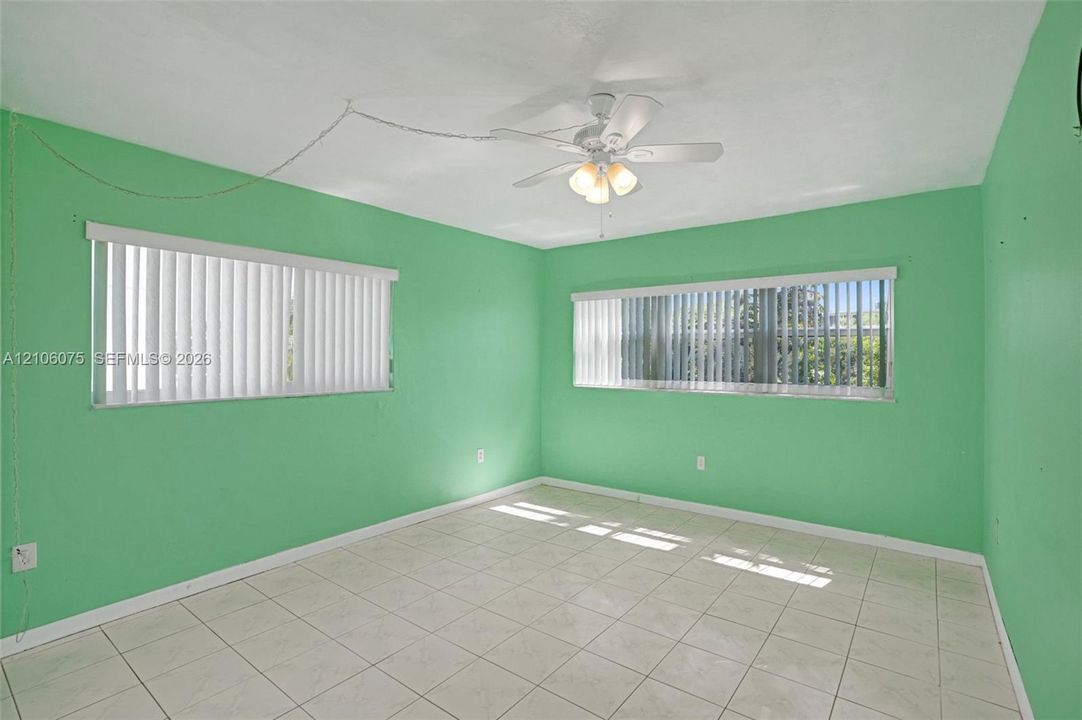 Room featuring tile flooring, two windows with vertical blinds, and a ceiling fan with light fixture