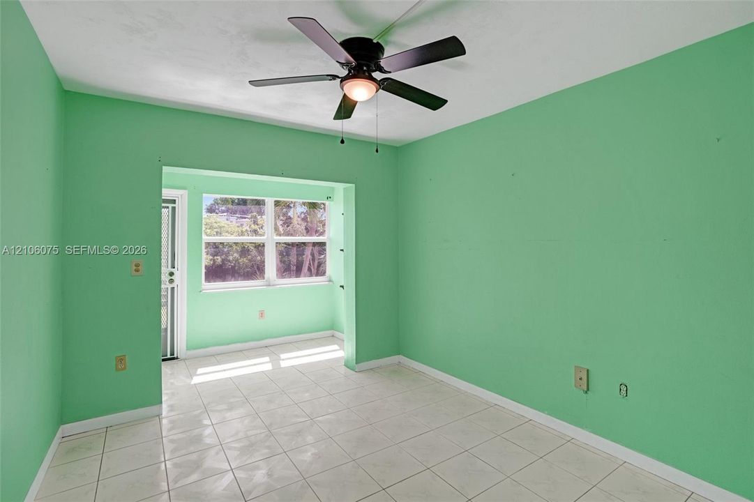 Interior space featuring light-colored tile flooring, a multi-pane window, and a ceiling-mounted light fixture with a five-blade fan