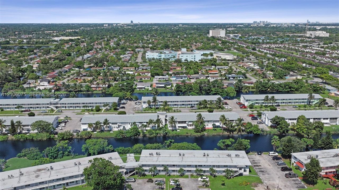 Aerial perspective of multi-family structures featuring paved surface parking, low-pitched rooflines, integrated balconies, and waterfront property positioning within a suburban landscape
