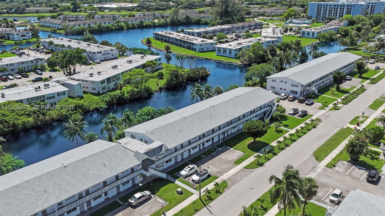 Aerial perspective featuring multi-story residential buildings, water frontage, landscaped grounds, and paved parking areas