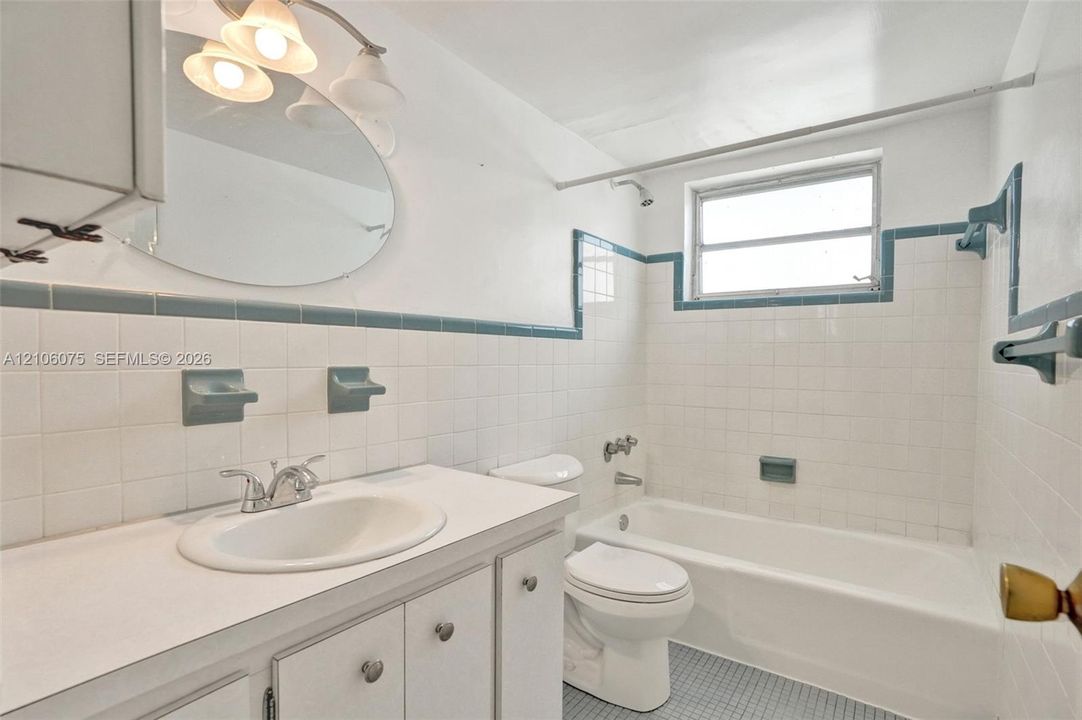 Bathroom featuring a white vanity with an integrated sink, oval wall-mounted mirror, ceramic wall tiling with decorative trim, and a bathtub with a shower combination