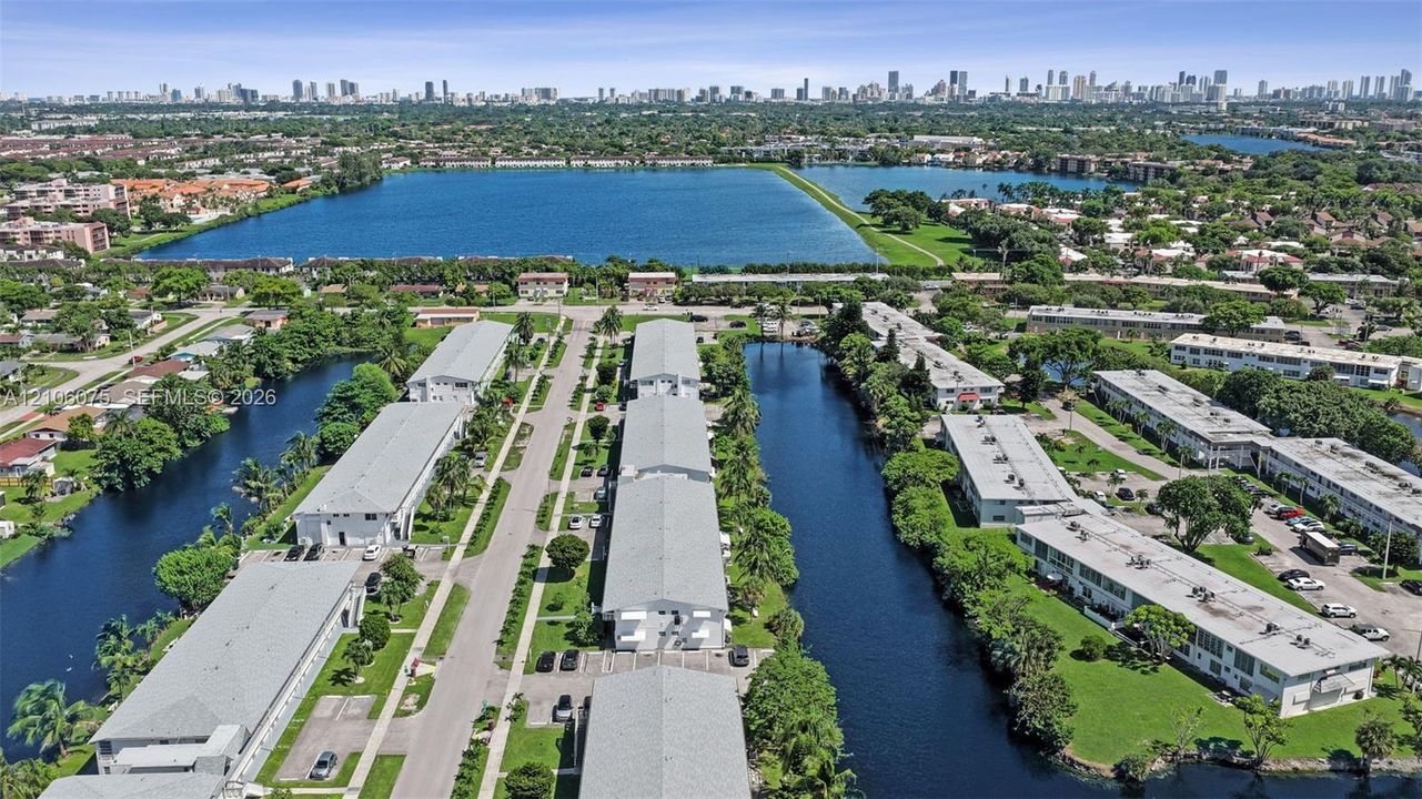 Aerial perspective featuring multi-unit structures, water-front positioning along canals, expansive green space, and urban skyline backdrop