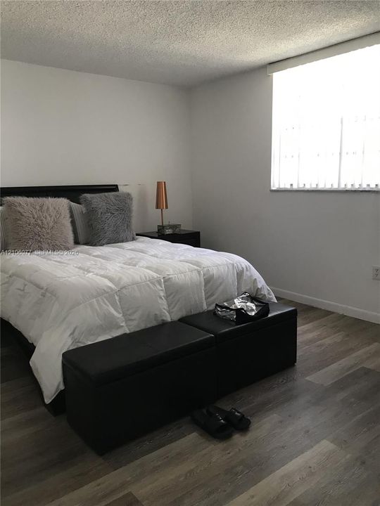 Room featuring wood-finish flooring, a large window with vertical blinds, and neutral wall tones