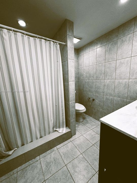 Bathroom featuring floor-to-ceiling tile, a built-in shower enclosure, square tile flooring, recessed lighting, and a vanity with a white countertop