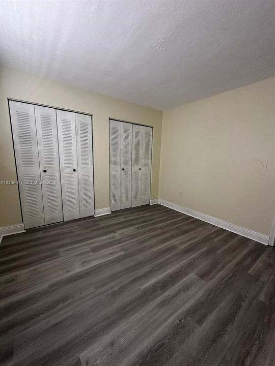 Wood-finish flooring, neutral wall tones, and dual louvered-style bi-fold closet doors