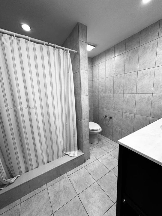 Bathroom featuring floor-to-ceiling ceramic wall tiling, recessed lighting, and a tiled shower partition