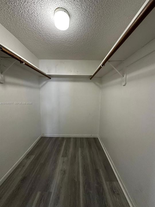 Storage area featuring wood-finish flooring, white walls, integrated shelving, and ceiling-mounted lighting