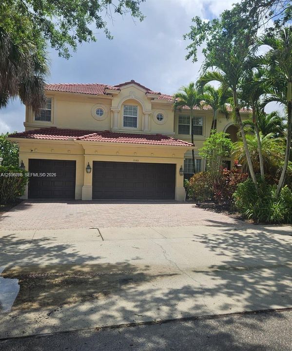 Two-story stucco exterior featuring a red tile roof, multi-car garage, arched window accents, and paved driveway