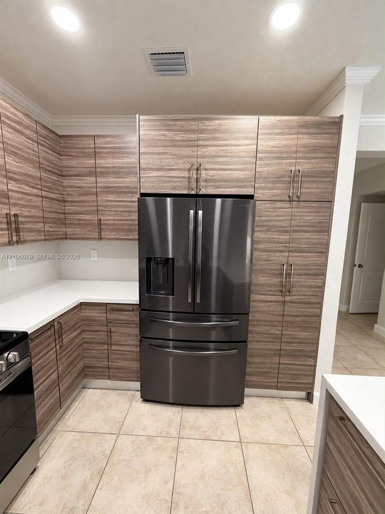 Kitchen featuring horizontal-grain wood cabinetry, ceiling-height pantry storage, white solid-surface countertops, recessed lighting, and a stainless steel French-door refrigerator