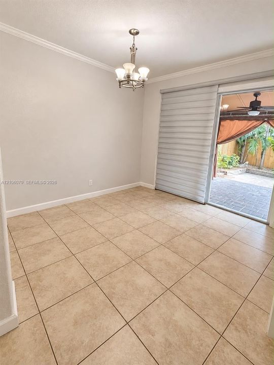 Neutral-toned tile flooring, crown molding, multi-light chandelier, and sliding glass door with integrated window treatments