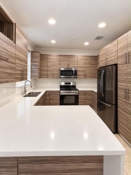 Kitchen featuring horizontal-grain wood-finish cabinetry, solid surface countertops, stainless steel appliances, and recessed lighting