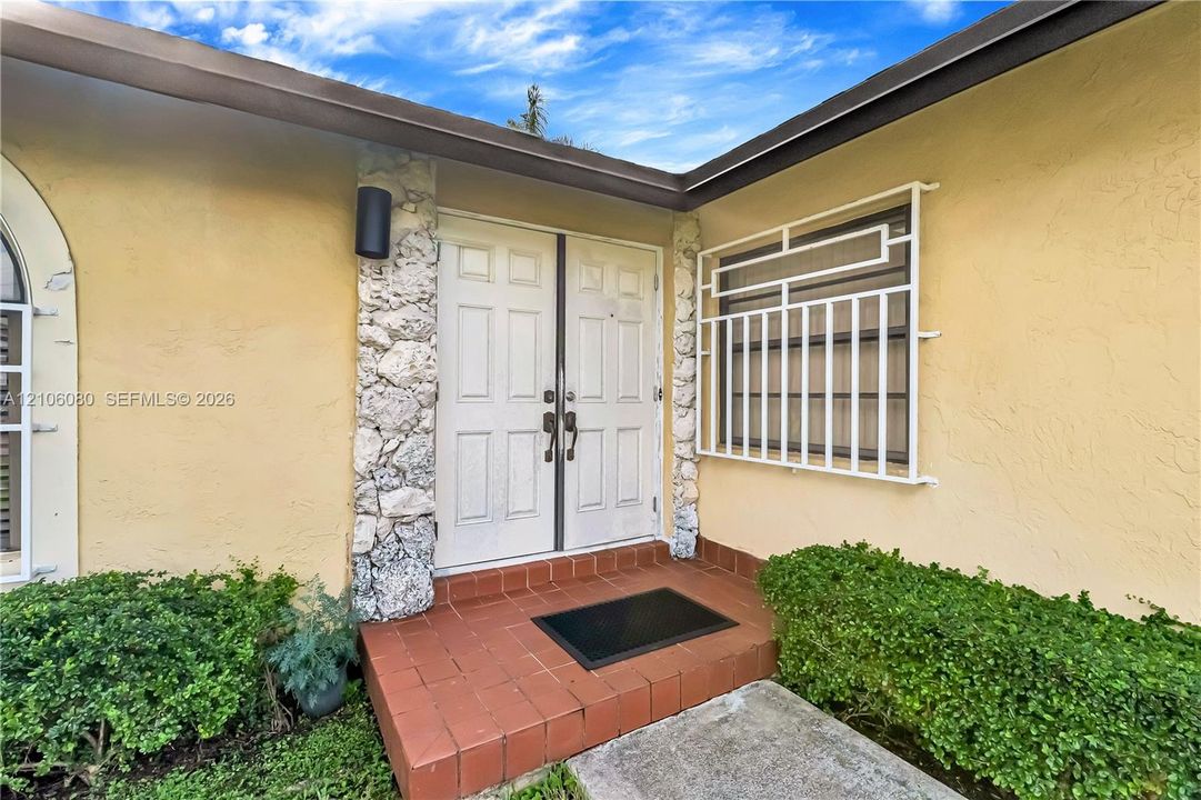 Entryway featuring double doors, stone-textured columns, red clay tile flooring, and a fixed geometric metal security grille