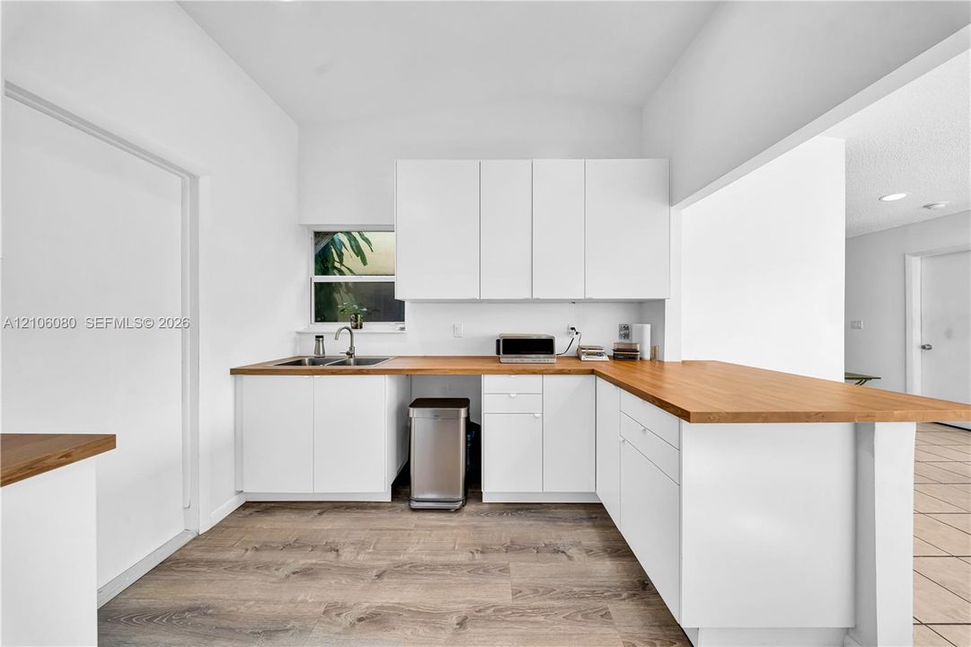 Kitchen featuring white cabinetry, wood-finish countertops, stainless steel dual-basin sink with gooseneck faucet, and wood-finish flooring