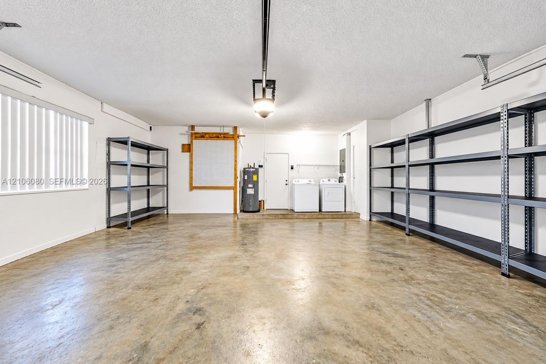 Garage featuring concrete flooring, ceiling-mounted automatic door opener, metal utility shelving, and laundry hookups