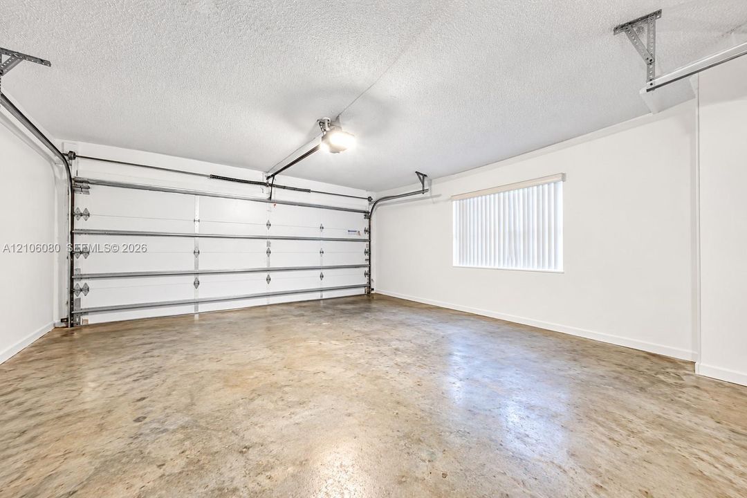 Attached garage featuring high-clearance overhead door, concrete flooring, and window with vertical blinds