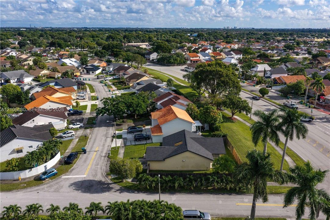 Aerial perspective of the residential property featuring a pitched shingle roof, paved driveway, expansive lawn, and mature palm trees