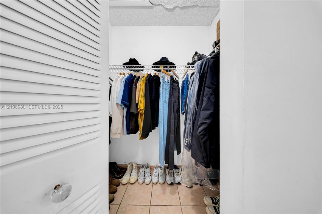 Reach-in closet featuring white louvered doors, wire shelving, and tiled flooring
