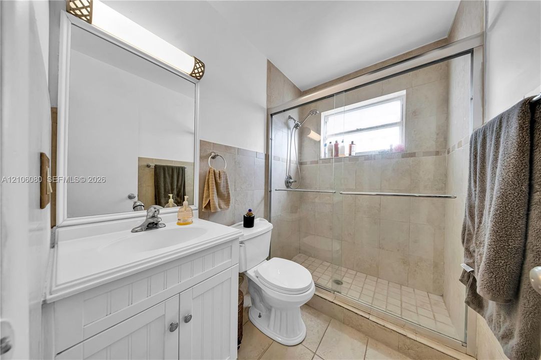 Bathroom featuring a white beadboard vanity, integrated sink, wall-mounted light fixture, and a walk-in shower with sliding glass doors and tiled surround