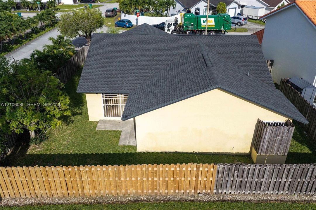 Exterior view featuring a shingled roof, stucco siding, a wood fence enclosure, and a concrete pathway