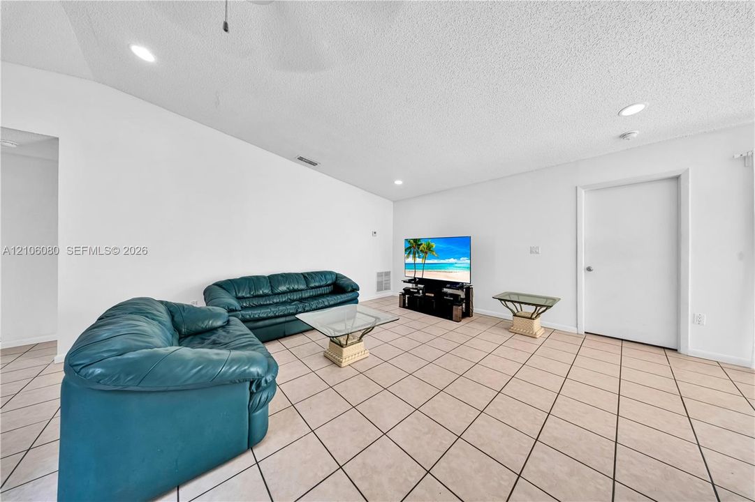 Spacious room featuring neutral ceramic tile flooring, vaulted ceiling, and recessed lighting
