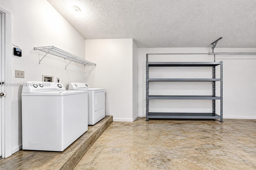 Utility space featuring a concrete floor, built-in wire wall shelving, and dedicated laundry hookups on a raised platform