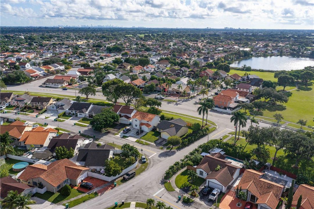 Aerial perspective of a suburban neighborhood featuring paved street infrastructure, multi-lot residential composition, established palm trees, and proximity to a central water feature