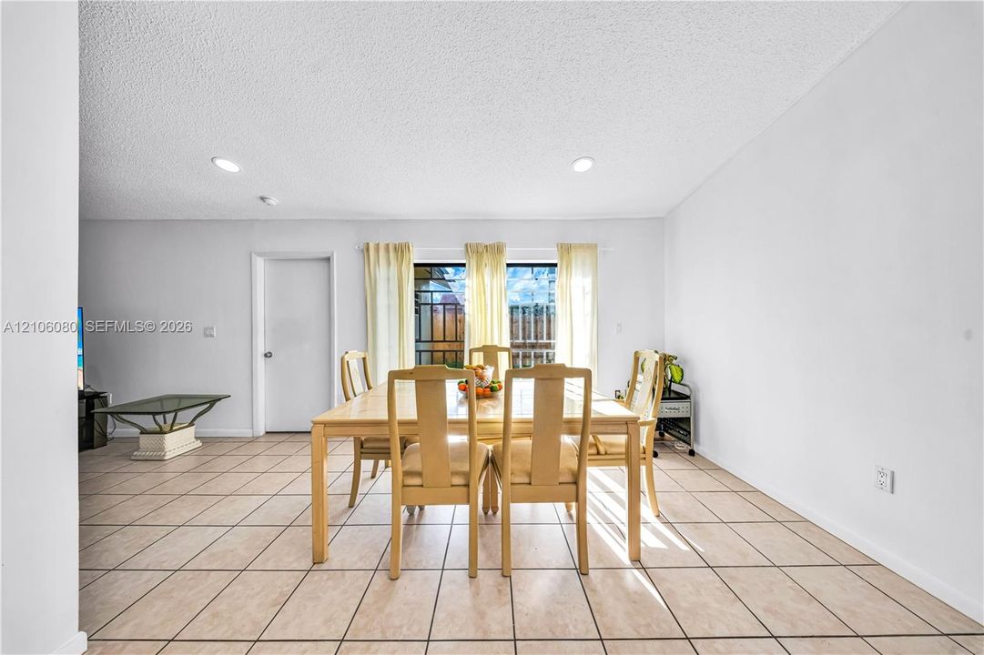 Open-concept room featuring light-toned tile flooring, recessed lighting, and a large sliding glass door with a security gate