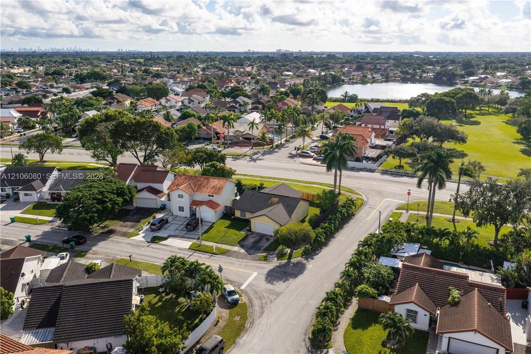Aerial perspective of a residential neighborhood featuring paved streets, mature palm trees, multi-roofline architectural styles, and proximity to a local lake