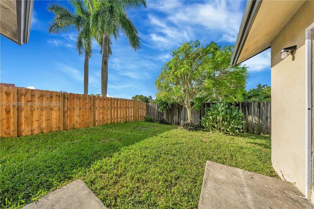 Fenced backyard featuring a manicured lawn, concrete patio, exterior wall-mounted light fixture, and mature landscaping