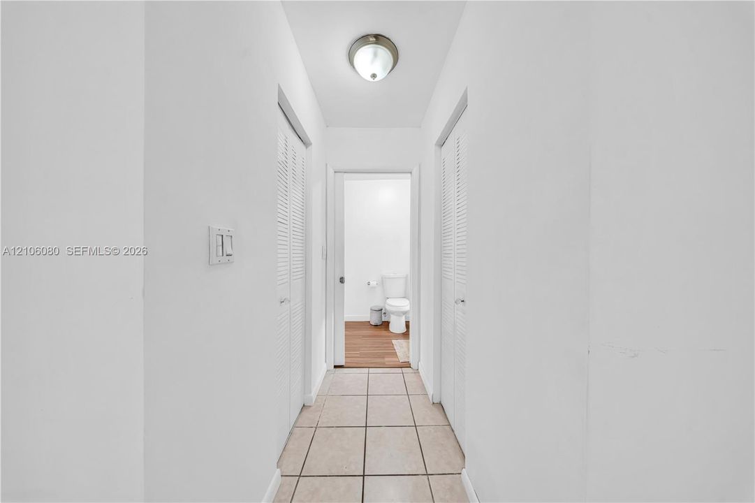 Hallway featuring ceramic tile flooring, two louvered closet doors, and a flush-mount ceiling light fixture