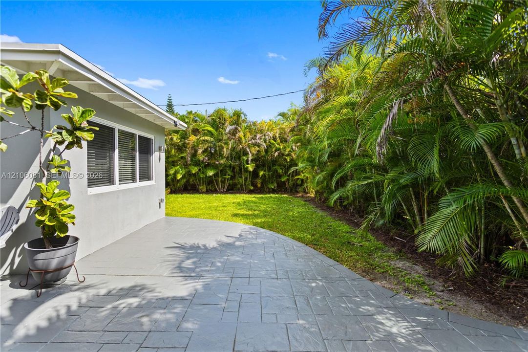 Stamped concrete patio featuring an expansive lawn, bordered by dense mature vegetation