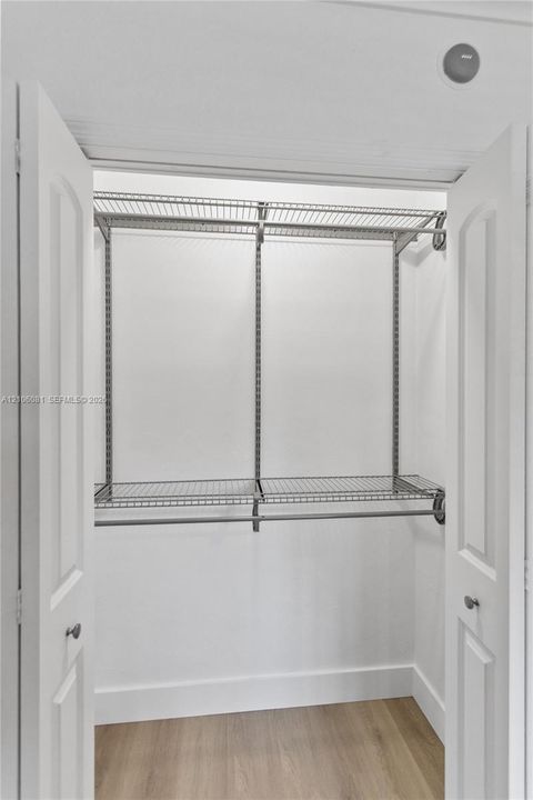 Storage closet featuring dual arched-panel doors, wire shelving, and wood-finish flooring