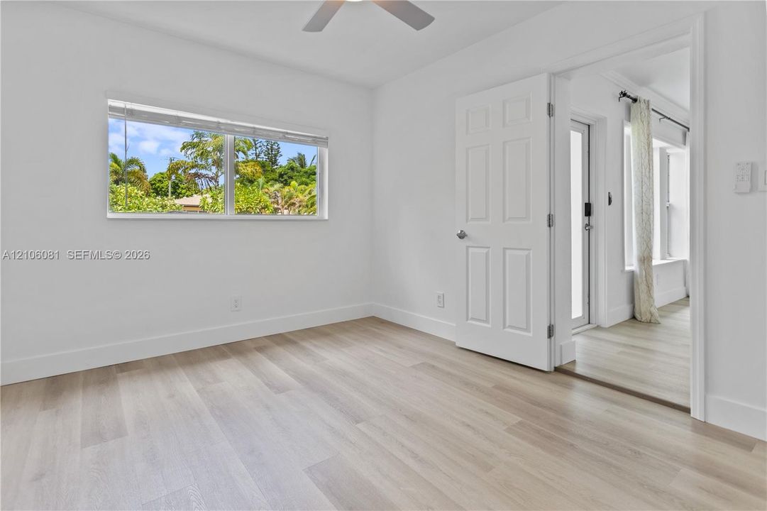 Interior space featuring wood-finish flooring, white walls, a ceiling fan, and a multi-panel door