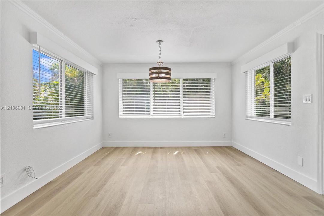 Light-filled room featuring wood-finish flooring, crown molding, a central drum pendant light fixture, and windows equipped with horizontal blinds