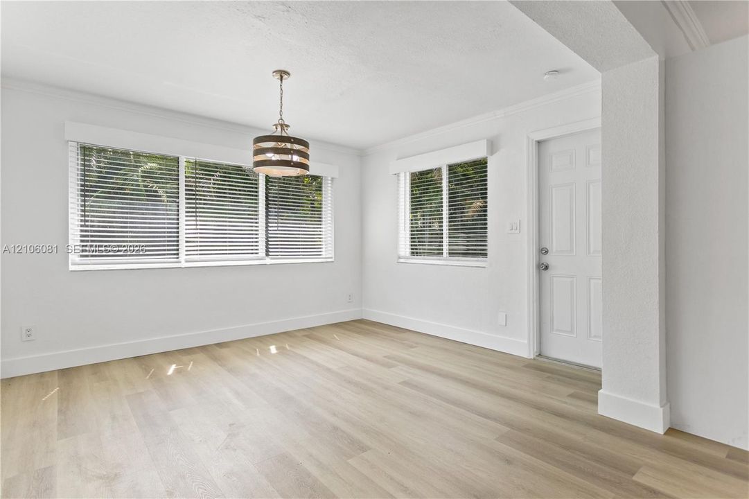 Interior space featuring wood-finish flooring, white walls, multiple windows with horizontal blinds, and a drum-style pendant light fixture