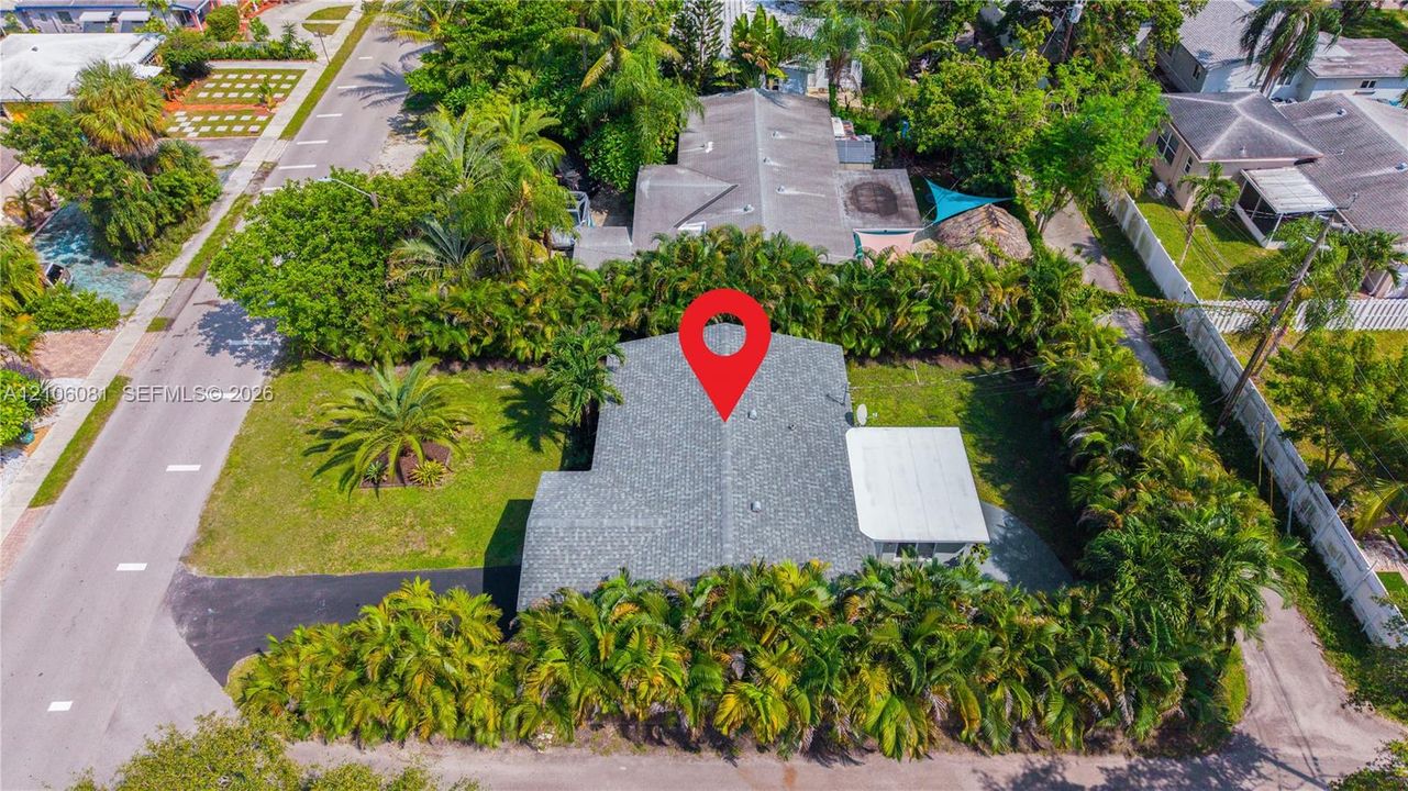 Corner lot featuring mature palm landscaping, asphalt driveway, and a covered patio area