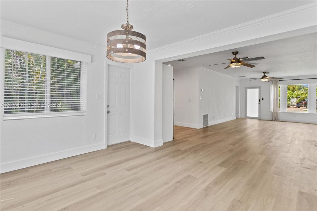 Neutral interior featuring wood-finish flooring, crown molding, a drum-style pendant light, and two ceiling fans