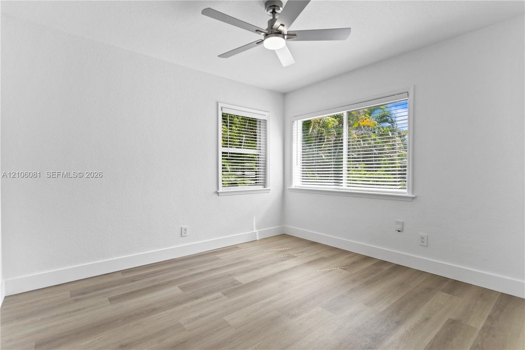 Room featuring wood-finish flooring, white walls, dual windows, and a brushed nickel ceiling fan with an integrated light fixture